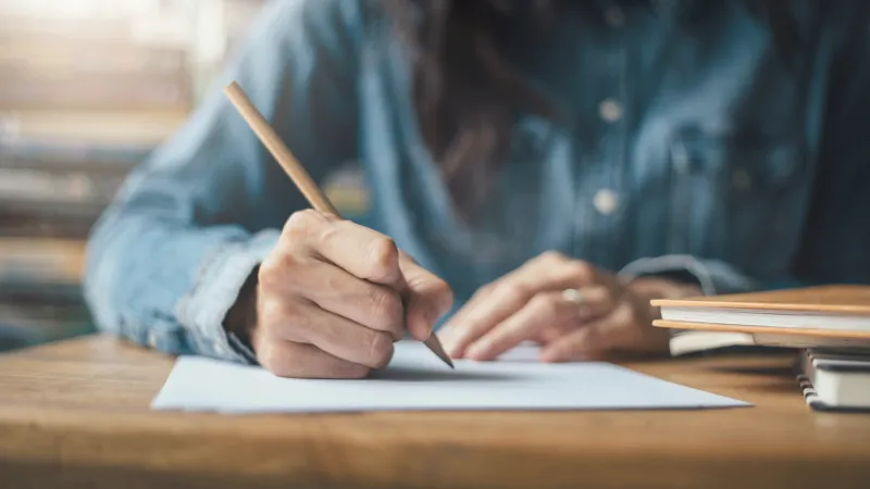 Eine Person schreibt mit Bleistift auf ein Blatt Papier