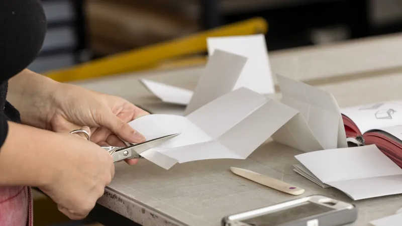 Eine Person schneidet an einem Arbeitstisch ein Papier zu.