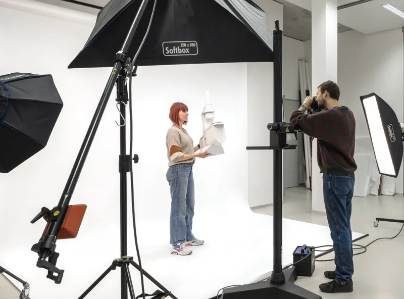 Ein Student fotografiert eine Studentin vor einem weißen Studiohintergrund 