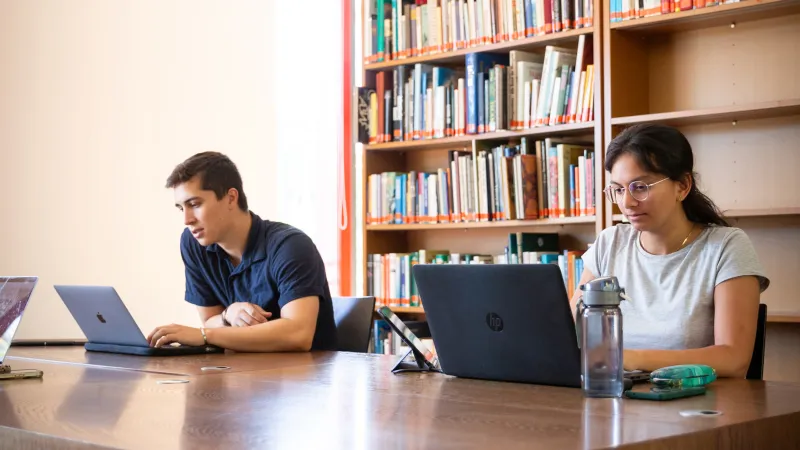 Zwei Studierende lernen in der Bibliothek an ihren Laptops