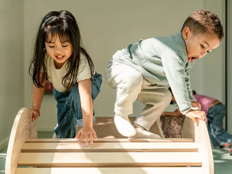 Zwei Kinder klettern auf einem Holzspielgerät in einem hellen Raum