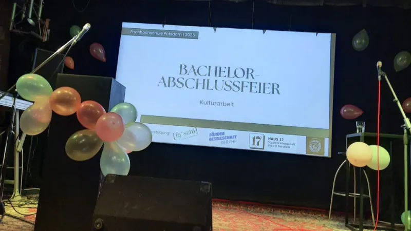 Foto einer Bühne mit Luftballons; auf den projizierten Folien steht "Bachelorfeier Kulturarbeit"