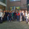 Eine Gruppe Studierender steht vor dem Hort Naturrfontein in Amsterdam, umgeben von Backsteinmauern und Fenstern mit einem bunten Baum-Logo.